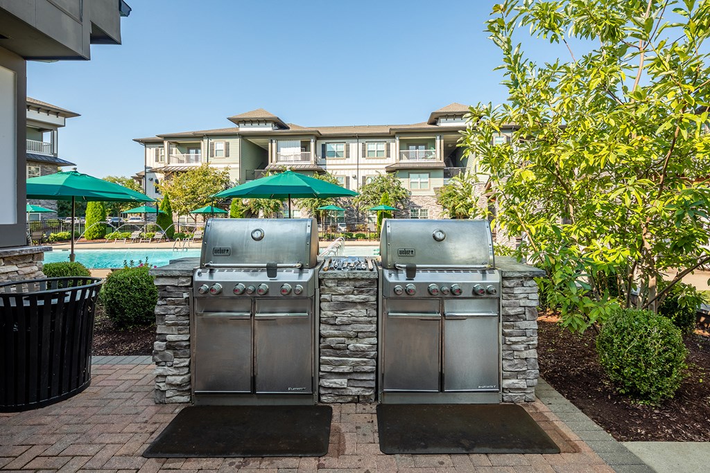 two stainless steel barbecue grills with umbrellas in the backyard of a house