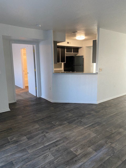 an empty living room with a kitchen in the background