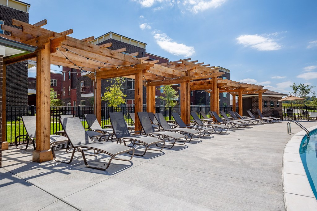 a row of chaise lounge chairs under a wooden structure next to a swimming pool