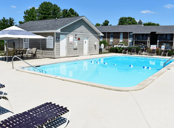 a large swimming pool with lounge chairs and umbrellas in front of a building
