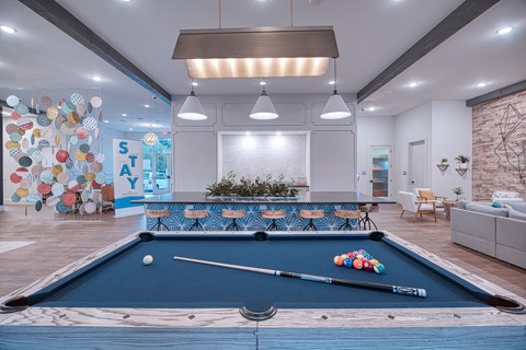 A pool table is in the middle of a room with a white wall and a plant in the background.
