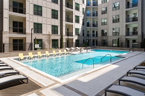 A large swimming pool surrounded by lounge chairs in front of a building.