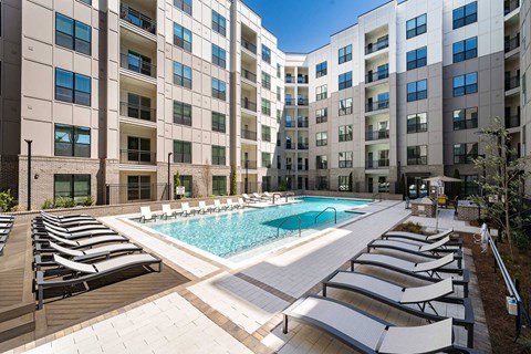 A large swimming pool surrounded by sun loungers in front of apartment buildings.