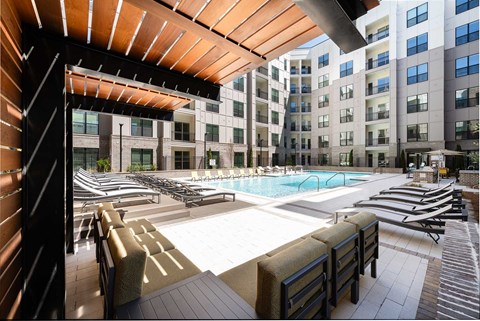 A large outdoor swimming pool surrounded by sun loungers and a wooden pergola.