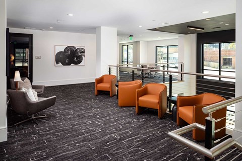 A black and white abstract painting hangs on a white wall above a row of orange chairs.