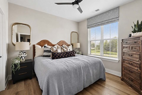 A bedroom with a bed, dresser, mirror, and window.