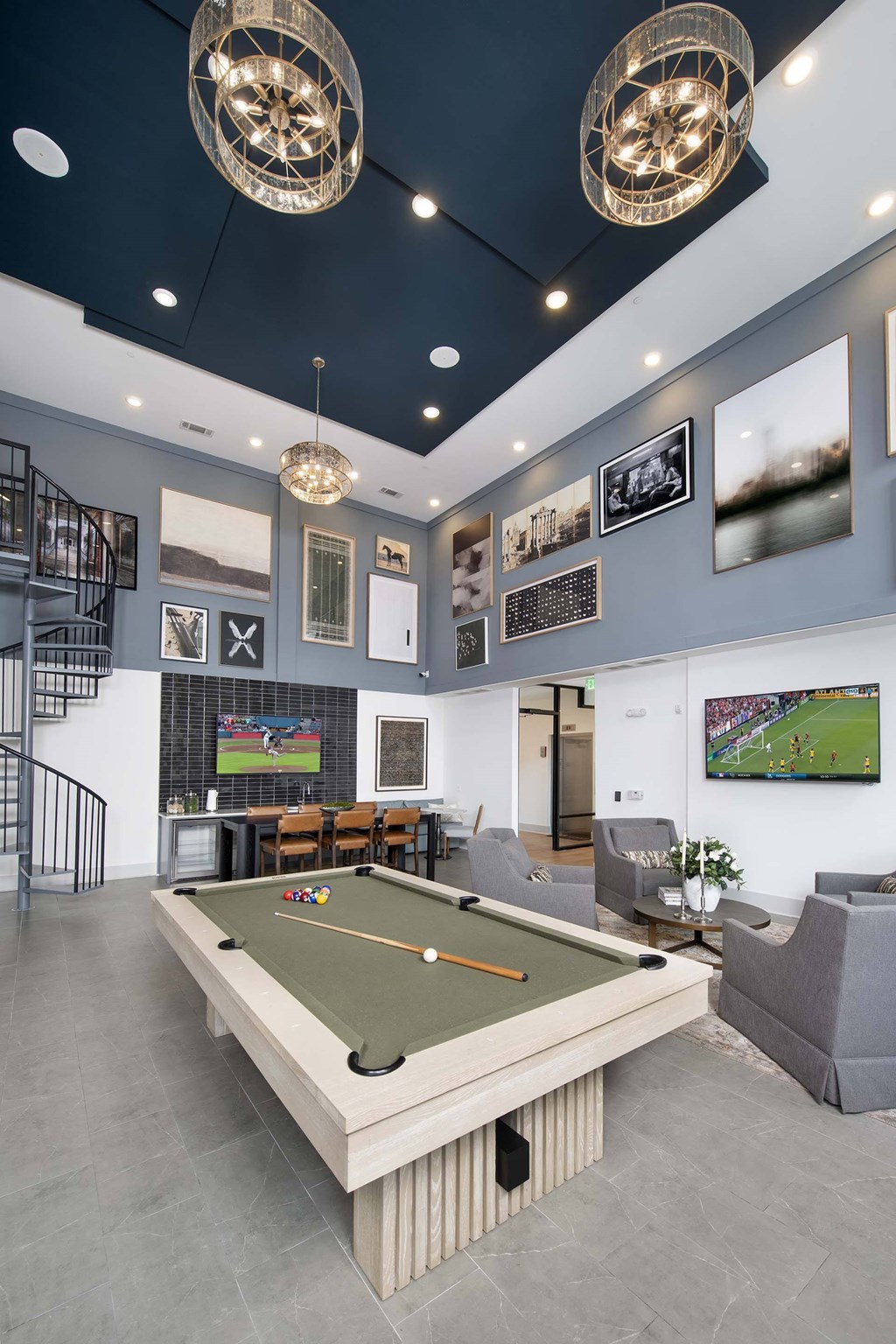 A billiard table is in the middle of a room with a grey couch and a TV.