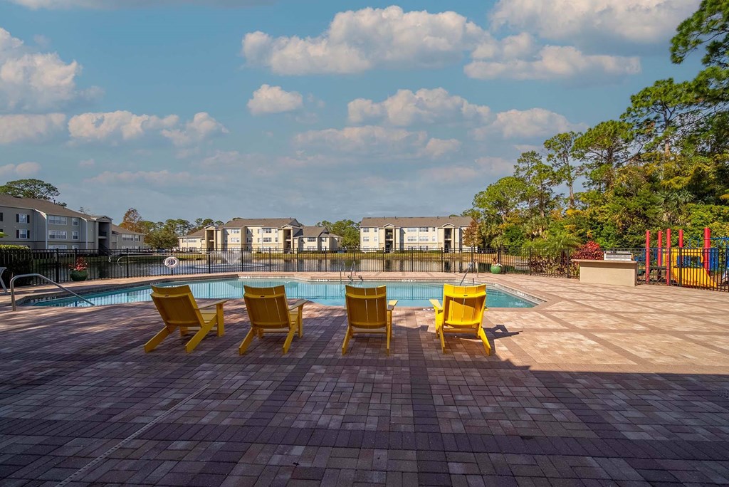 A pool area with yellow chairs and a red playground.