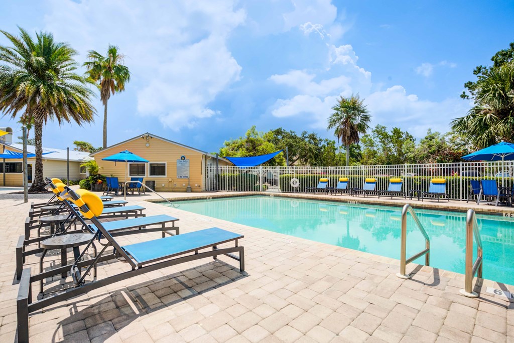 A pool area with sun loungers and a yellow building in the background.