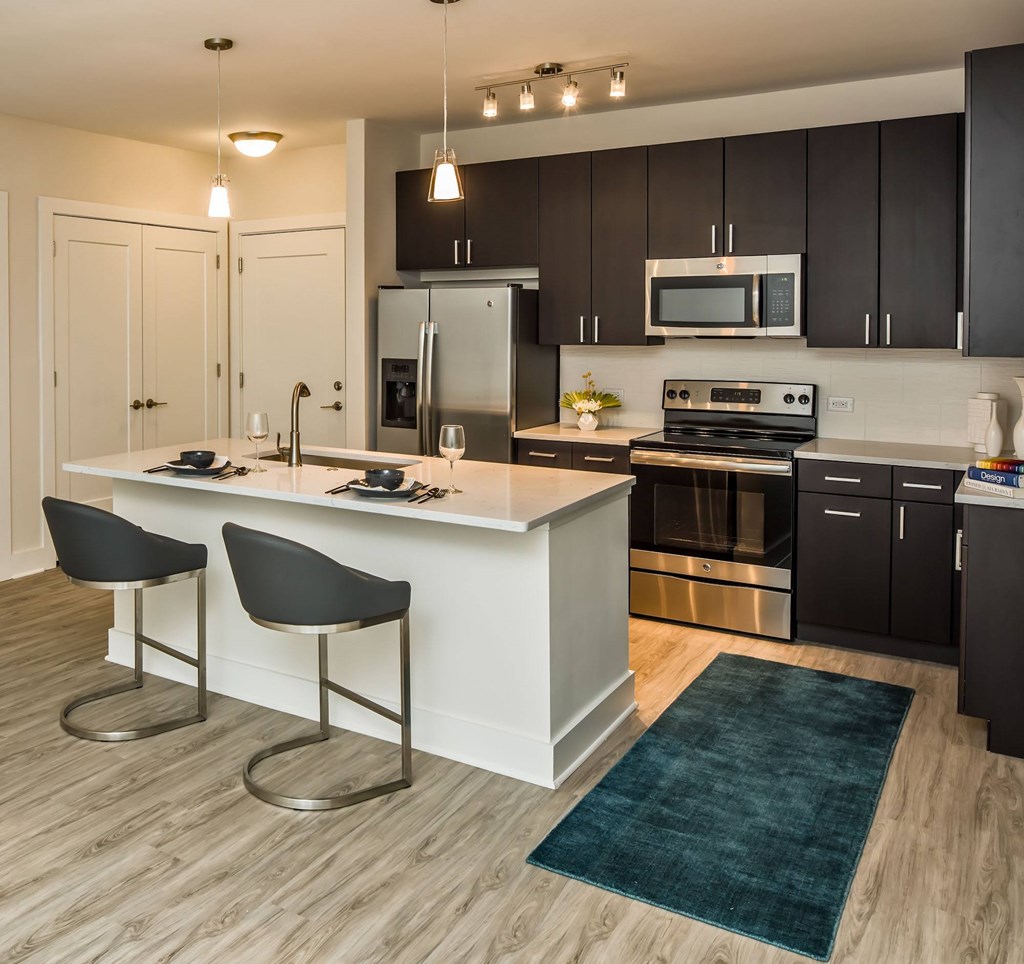 A modern kitchen with a white island and black chairs.