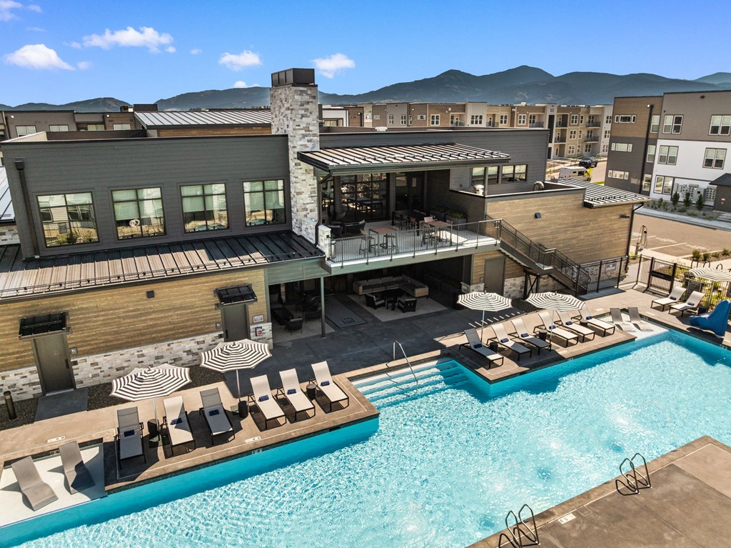 A large outdoor swimming pool with lounge chairs and a building with a balcony overlooking the pool.