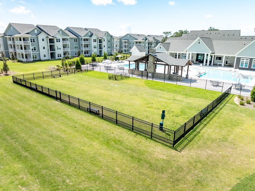 A black fence surrounds a green lawn in front of apartment buildings.