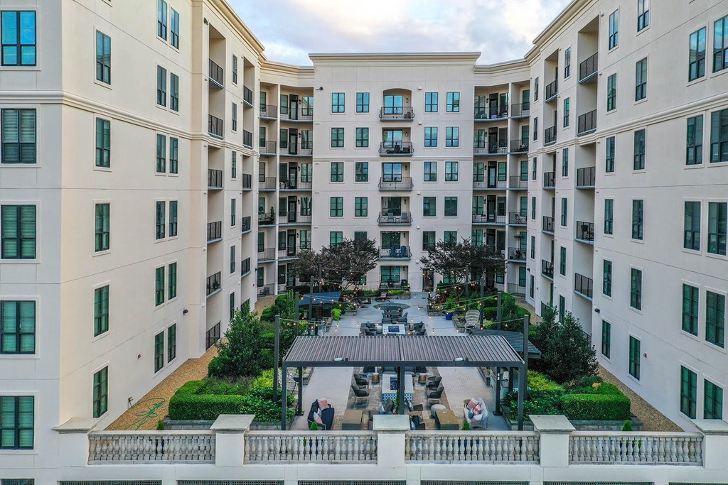 Buckhead, GA, Luxury Apartments - 92 West Paces - White Building Exterior with Outdoor Courtyard, Hedges, Cafe Lights, Lounge Seating, Fire Pits, Tables and Chairs, Grill Stations, and Pergola.