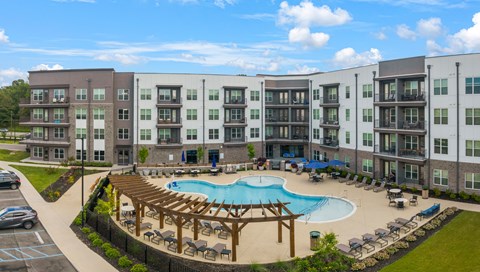 Studio Apartments in Chattanooga, TN - Populus Waterside - Resort-Style Swimming Pool With Lounge Seating, Pergola Shade, Blue Umbrellas, And Modern Apartment Exteriors.