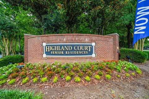A sign that says Highland Court Senior Residences in front of some trees.
