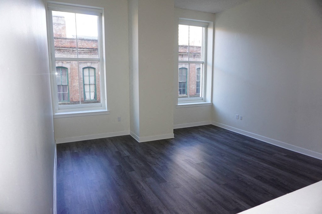 an empty living room with wood floors and two windows