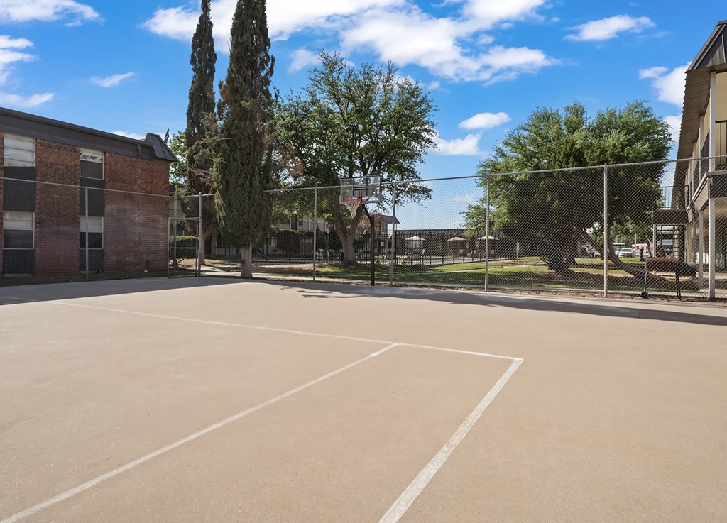 A large, empty parking lot with a building and trees in the background.