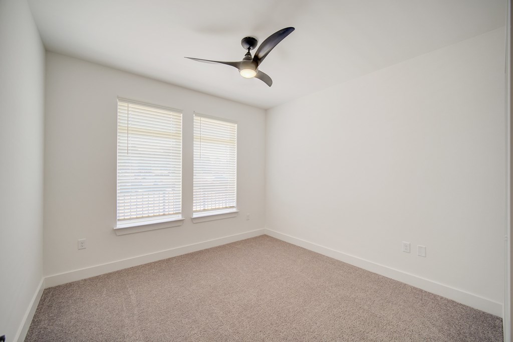 A room with a ceiling fan and two windows.