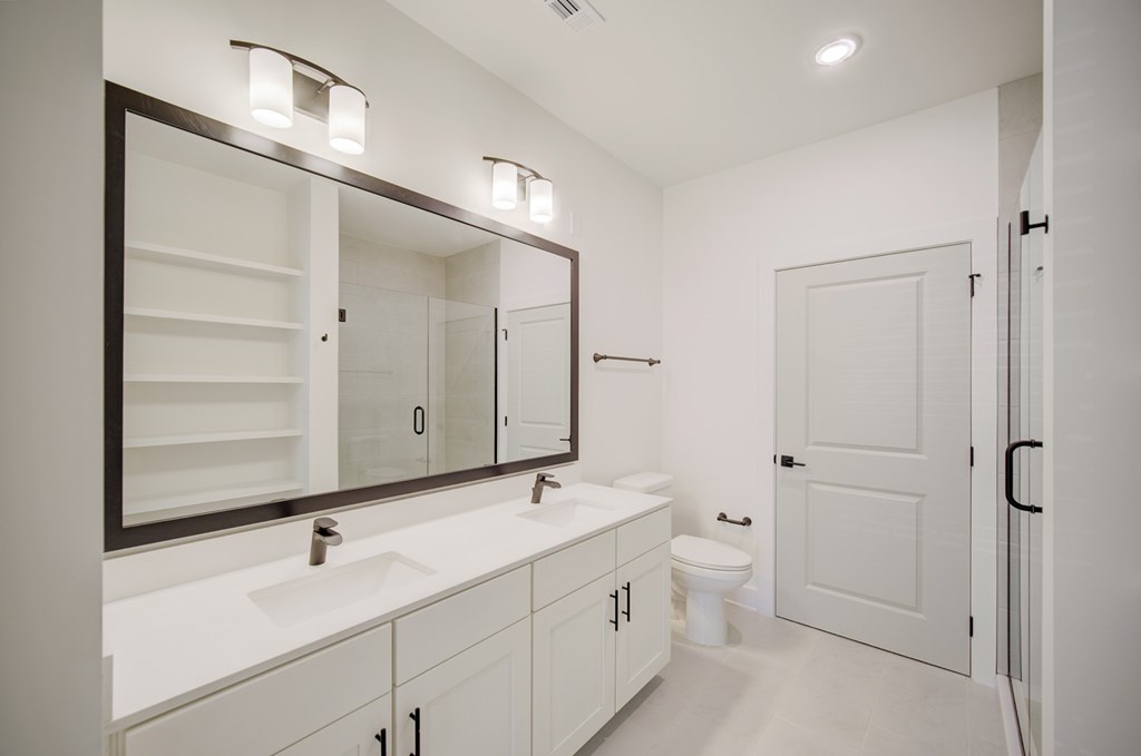 A white bathroom with a sink, mirror, toilet and a door.