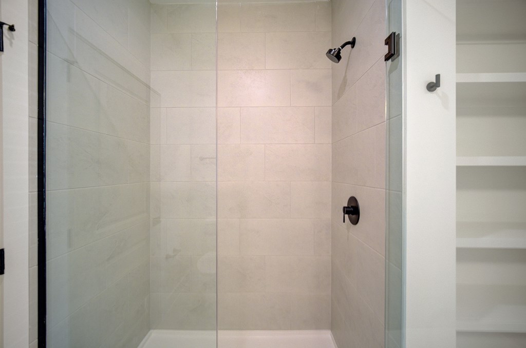 A white tiled shower with a glass door and a black handle.