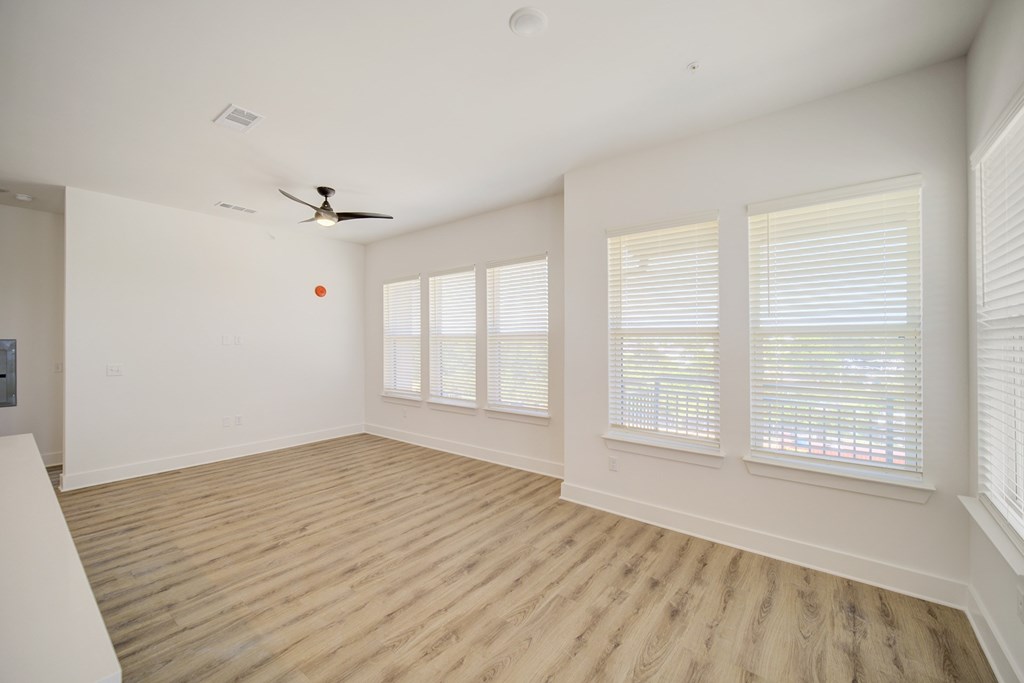 A room with a ceiling fan and three windows with blinds.