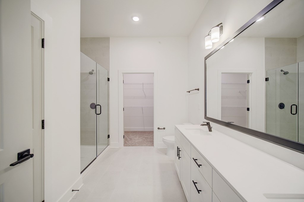 A white bathroom with a large mirror and a walk-in shower.