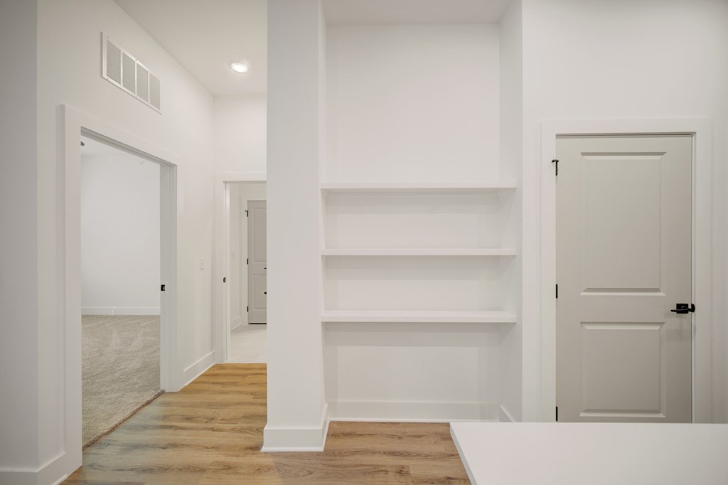 A white hallway with a door on the right and a shelf on the wall.