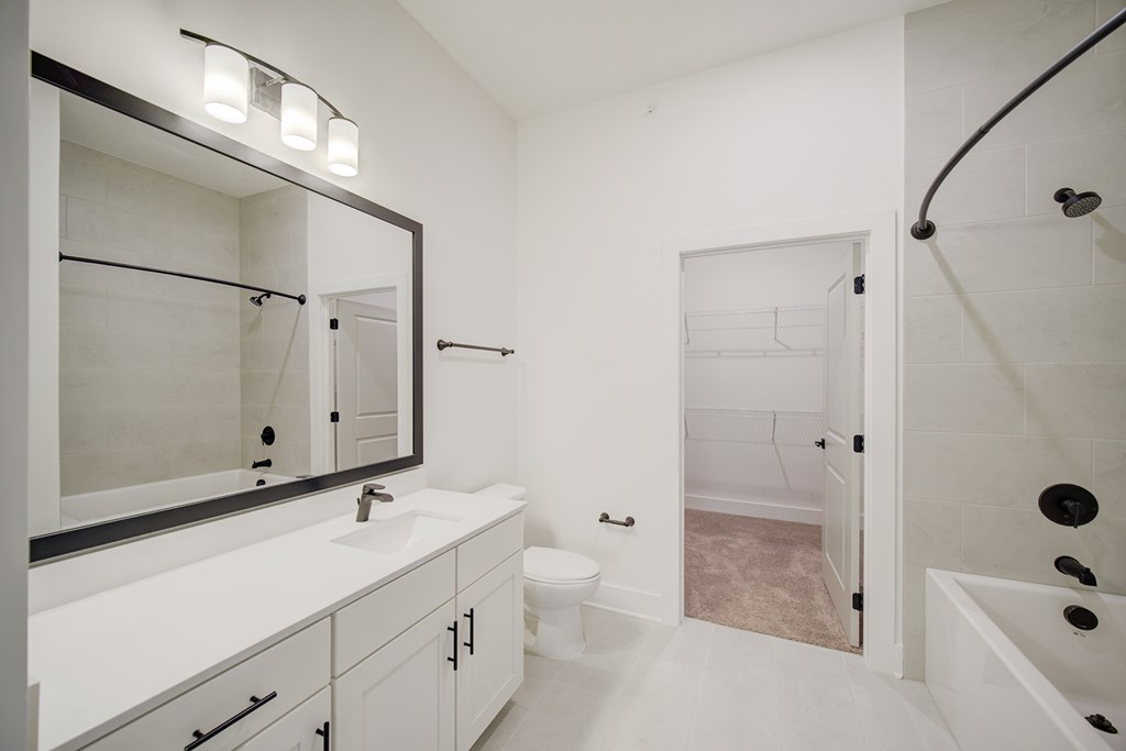 A white bathroom with a sink, mirror, toilet and bathtub.