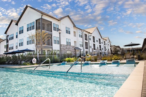 A swimming pool in front of a white building with blue umbrellas.