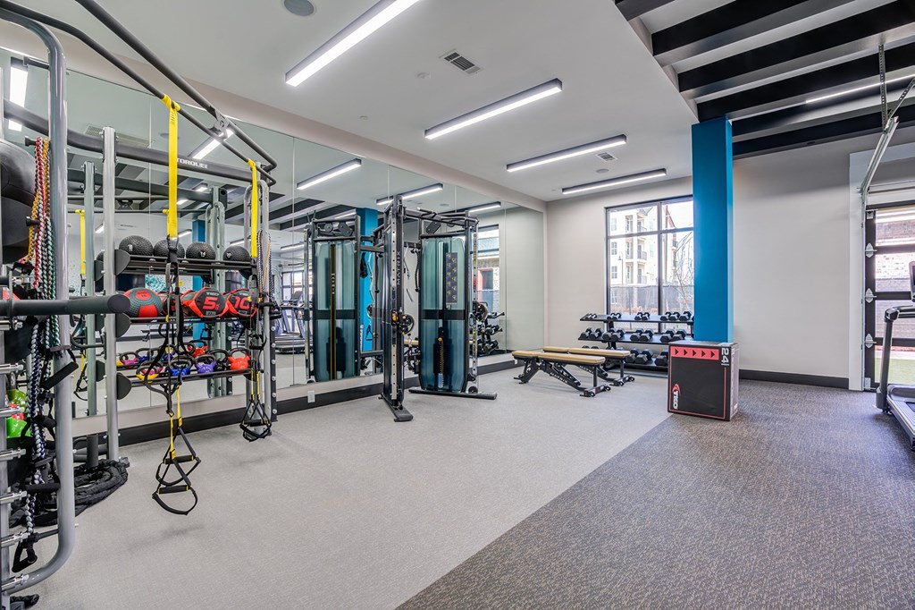 Madison, Alabama, Apartments with In-Unit Washer and Dryer - The Dempsey - Spacious Gym with Free Weights, Strength Training Equipment, Workout Benches, Mirror Wall, High Ceilings, and Sleek LED Lighting.