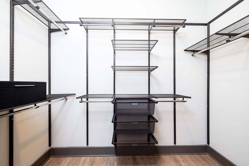 A black shelving unit with wire shelves and a black drawer is in a room with white walls.