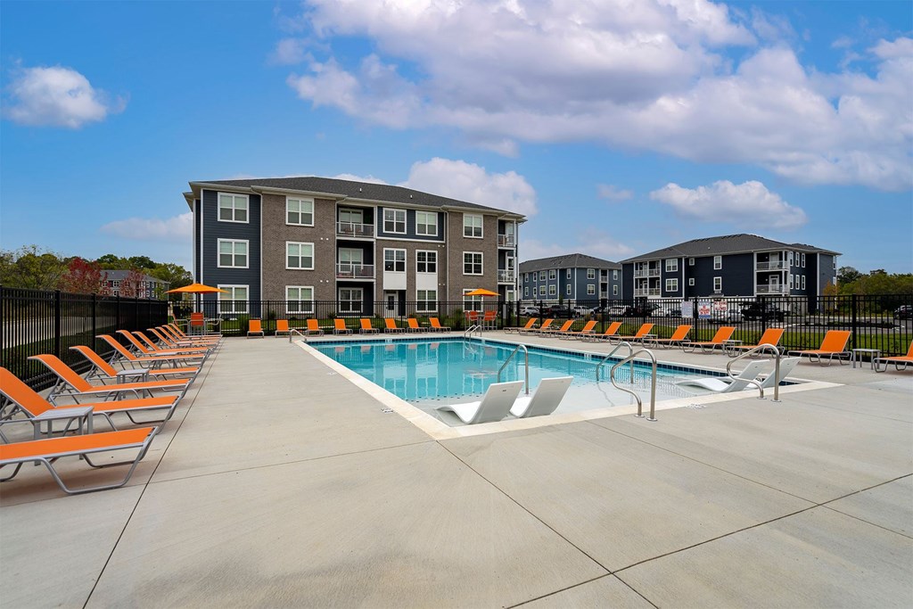 A swimming pool surrounded by orange lounge chairs in front of apartment buildings.