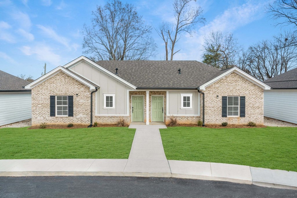 a white brick house with green doors and a lawn