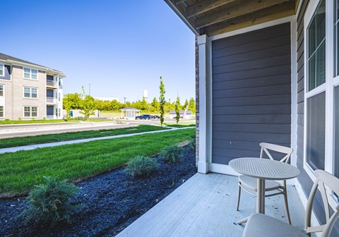 A patio with a table and chairs overlooks a grassy area and apartment buildings.