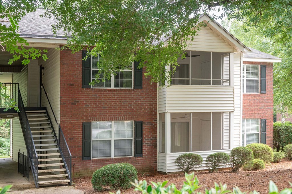 A house with a red brick wall and a white siding wall with green shutters.