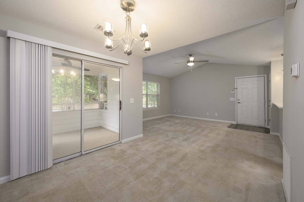 A room with a chandelier, sliding glass doors, and a carpeted floor.