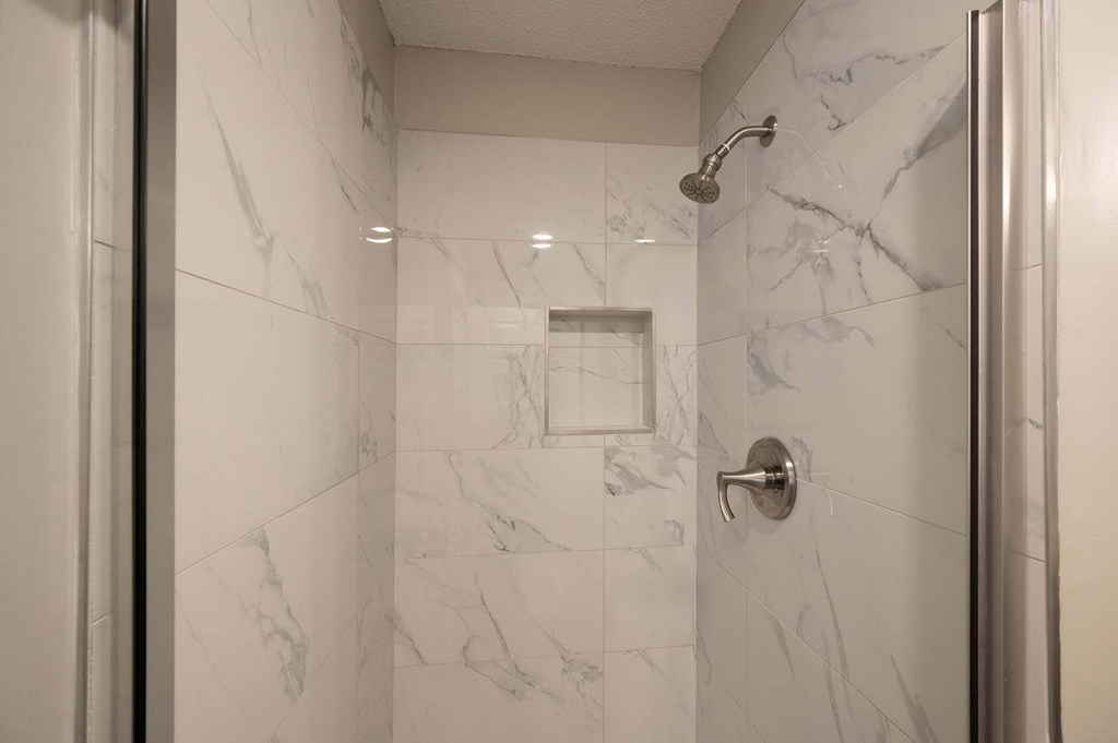 A white marble bathroom with a shower and a door.