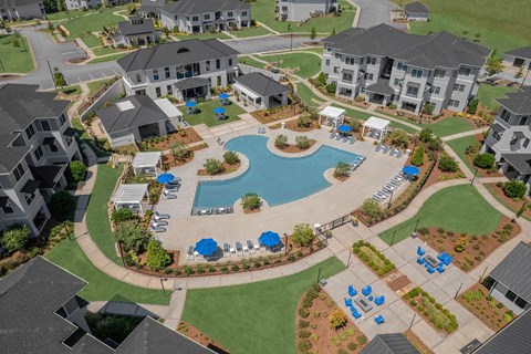 A large swimming pool surrounded by blue lounge chairs and umbrellas is the centerpiece of a resort-style community.