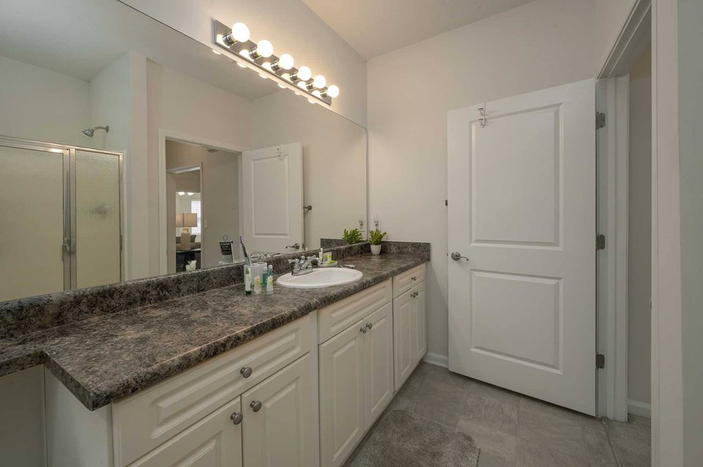 A bathroom with a sink, mirror, and a door.