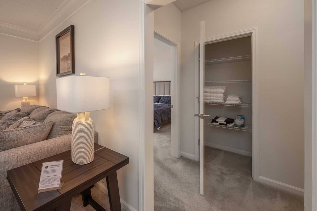 A lamp sits on a table in a room with a bed in the background.