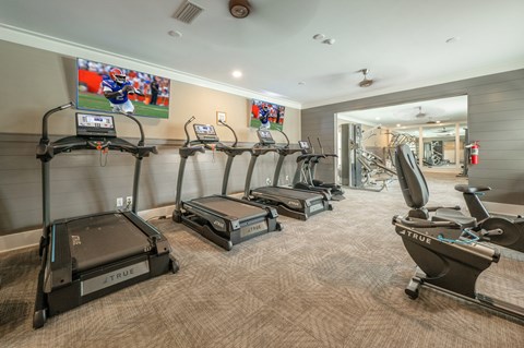 A gym with treadmills and a television showing a football game.