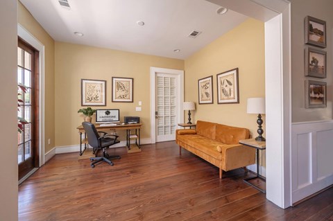 A living room with a yellow couch and a desk with a laptop.