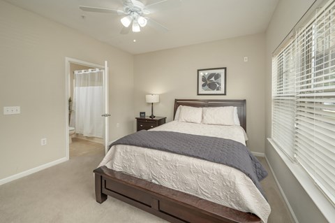 A bedroom with a bed, nightstand, and window with blinds.