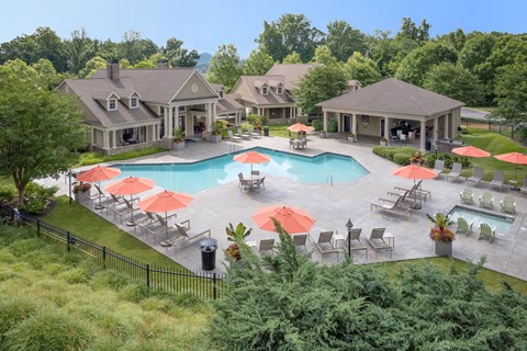 A large outdoor swimming pool surrounded by red umbrellas and lounge chairs.
