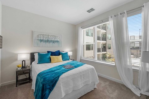 Luxury Apartments Near Museum Sunken Gardens - Gallery 3100 - A Bright Bedroom With Teal And Yellow Accents, White Sheer Curtains, And A Large Window Overlooking The Community.