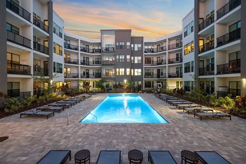 St. Petersburg, FL Pet-Friendly Luxury Apartments - Gallery 3100 - A Rectangular Glowing Blue Pool Centered In A Modern Apartment Courtyard At Twilight, Surrounded By Lounge Chairs.