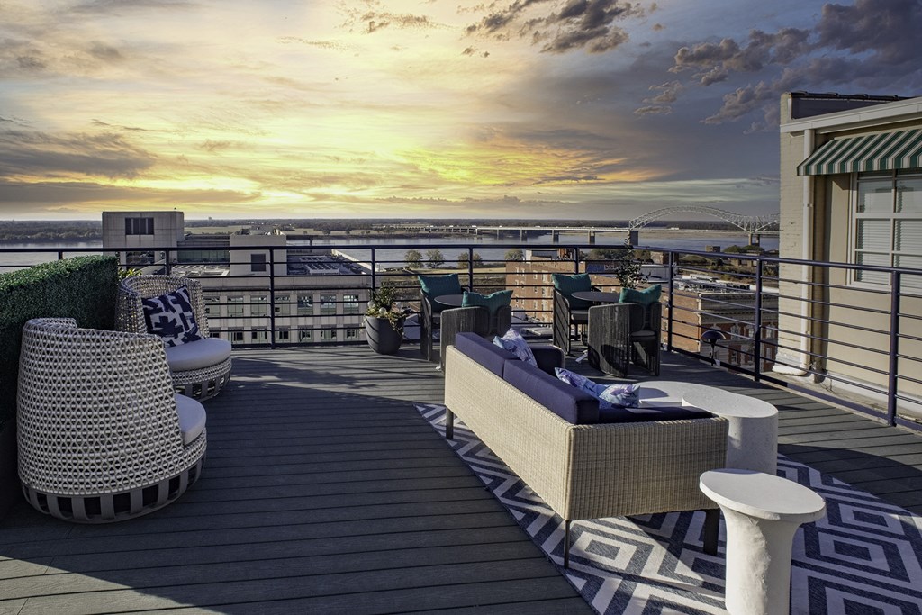 a rooftop deck with furniture and a sunset over the ocean