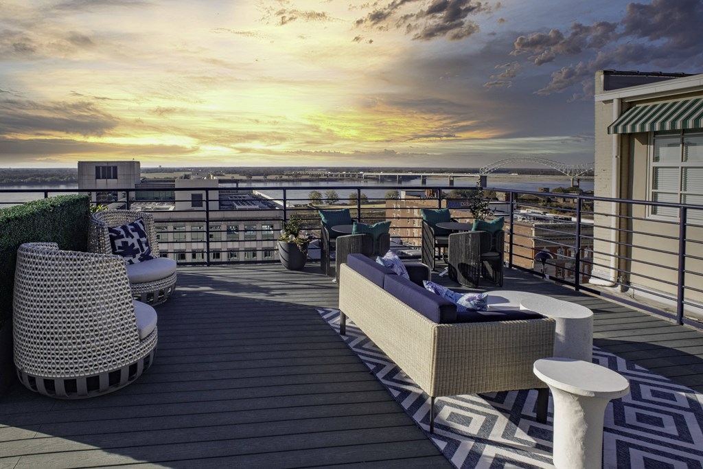 a rooftop deck with couches and chairs overlooking the ocean and a sunset