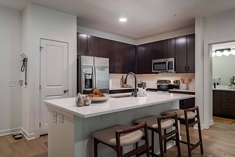 A kitchen with a white counter top and brown chairs.