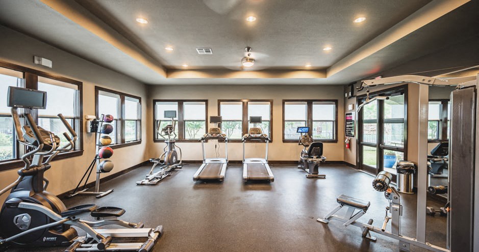 a gym with cardio machines and weights on the floor and windows